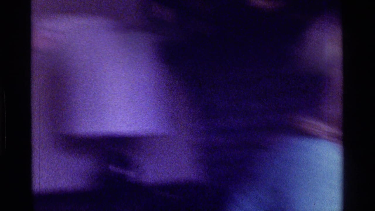 Blurred interior view with dark shapes and a pale object in low purple light.
