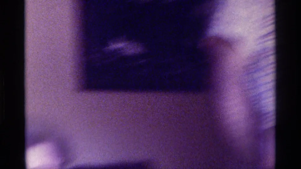 A shaky 1970s Kentucky home-movie frame shows a wall, a dark upper form, and a vertical edge in a low-lit private room.