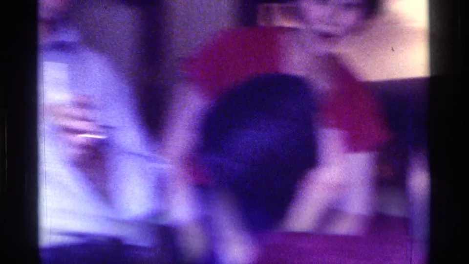 Several adults appear close together in a dim Kentucky room, including a person holding a glass, captured with 1970s home-movie blur and purple color cast.