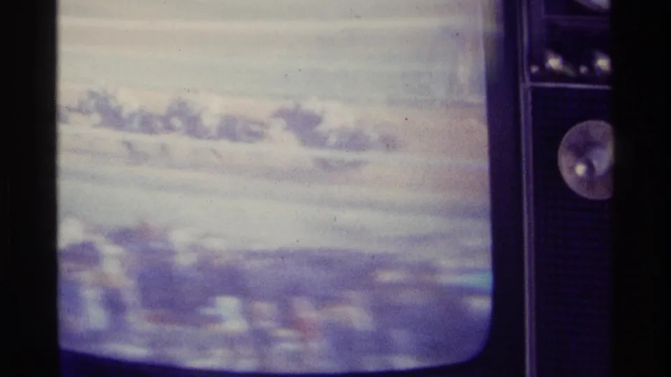 A television cabinet with visible control area frames a soft broadcast view of horses racing along a track.