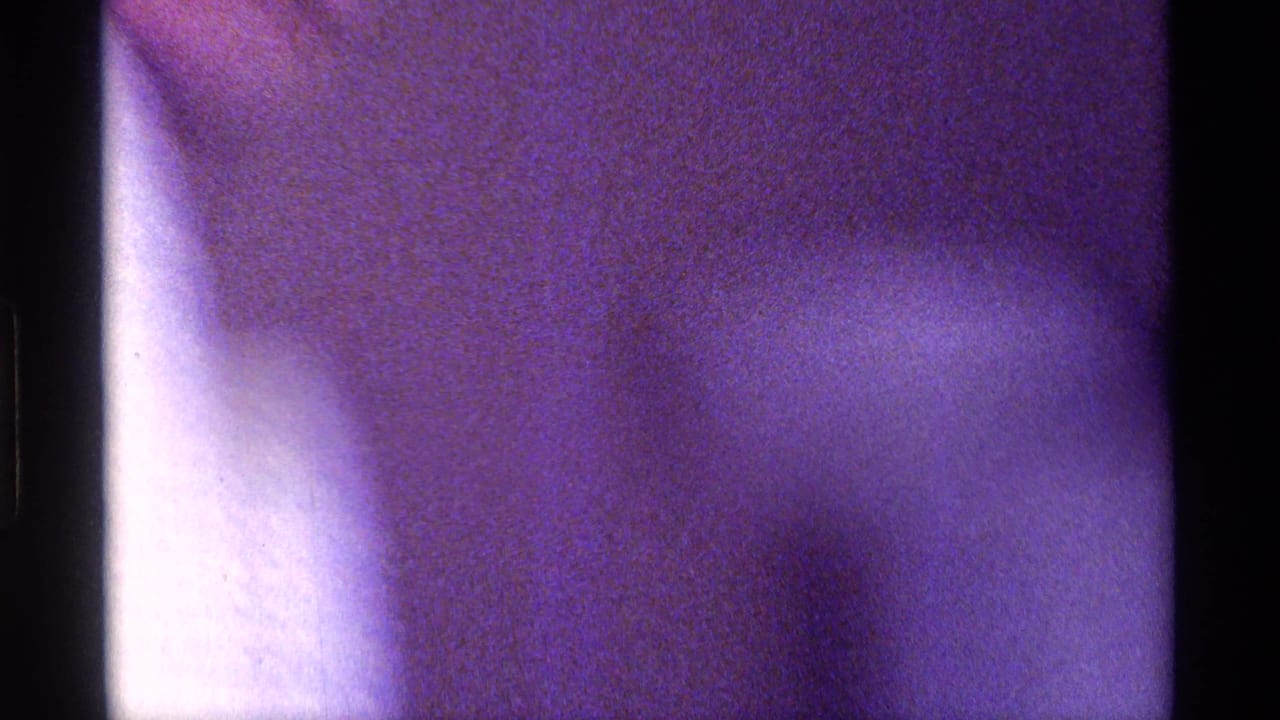 Motion-blurred 8mm frame from the Kentucky clip, with an indistinct close figure and strong purple color cast.