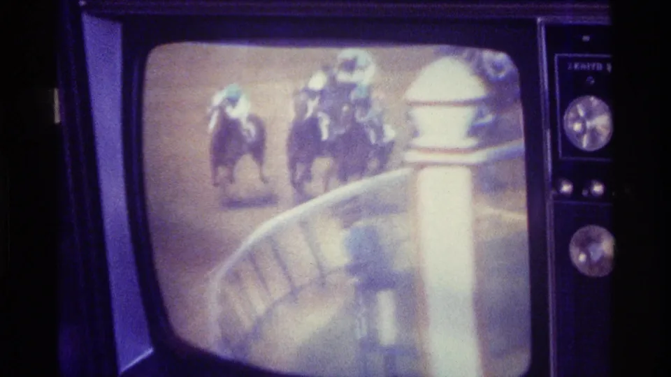 A vintage television set in a private Kentucky home shows a horse race with jockeys visible on the screen in grainy 1976 8mm footage.