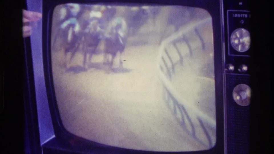 The television screen shows horses and jockeys moving along a racecourse railing, captured from a 1976 Kentucky home interior on 8mm film.