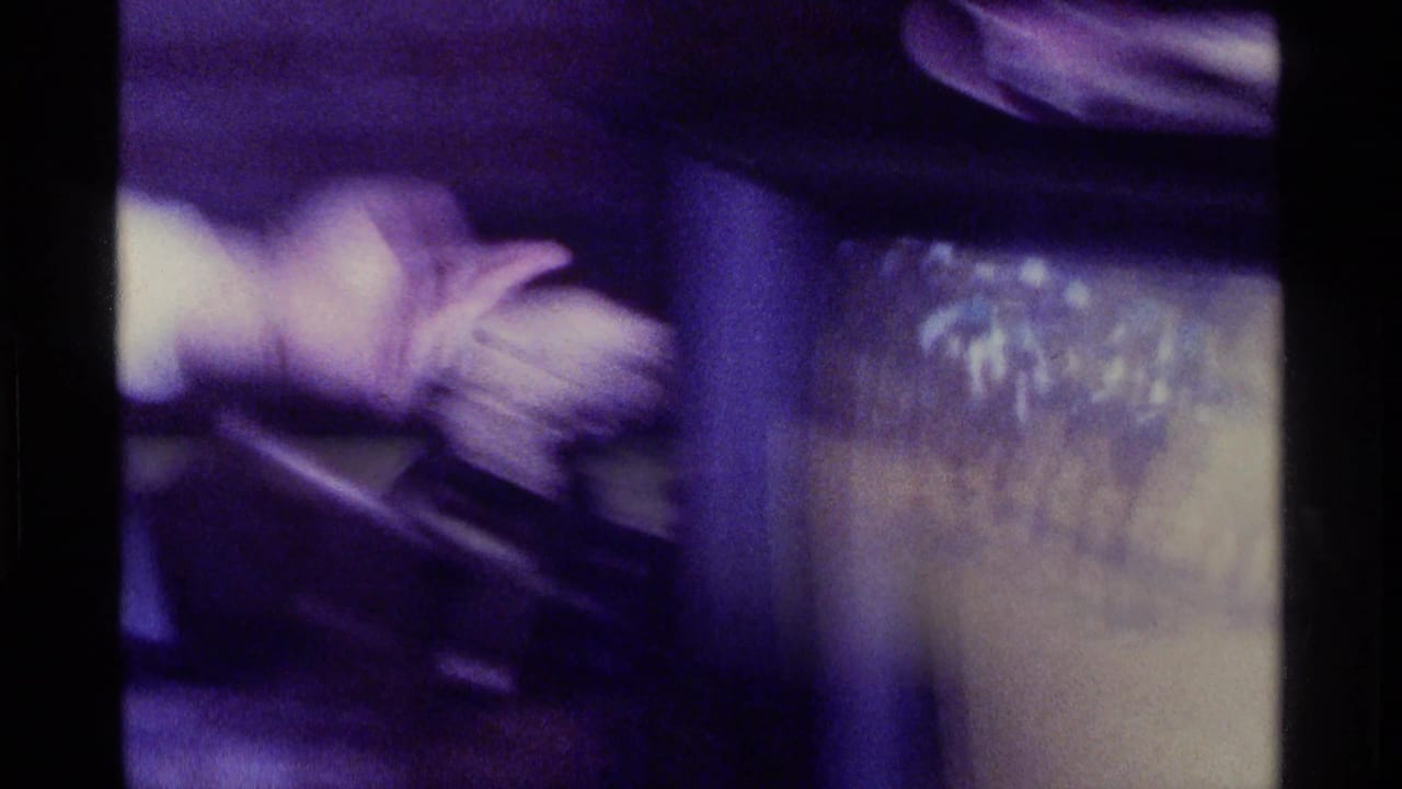 A blurred adult arm gestures near a television set in a dim Kentucky home interior, consistent with the supplied 1976 8mm footage metadata.