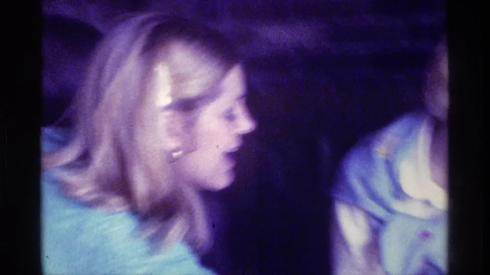 Two adult women sit close together in a dim Kentucky home interior, with soft focus and purple-blue 8mm color obscuring some facial detail.