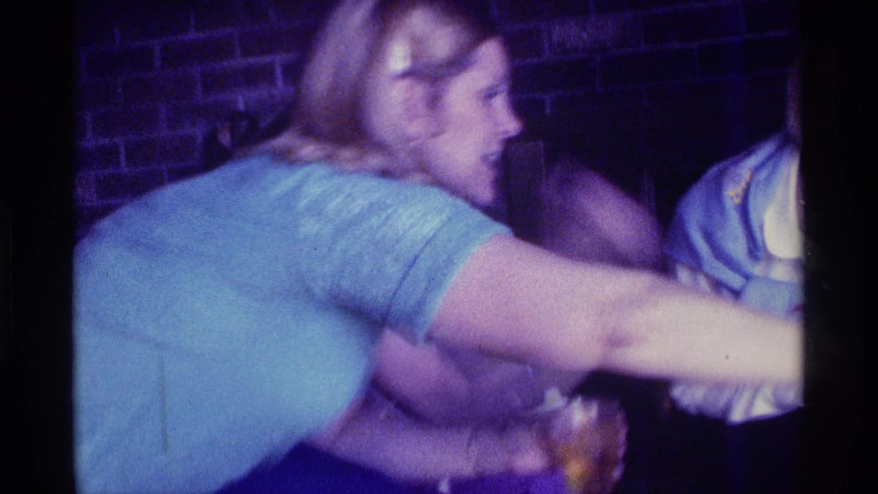 Woman in a blue shirt reaches across a dim room while laughing.