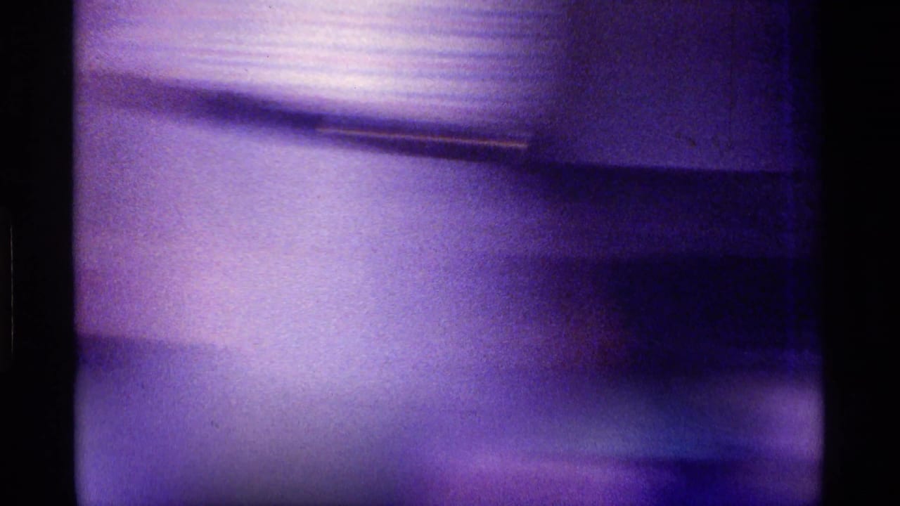 Blurred purple-toned frame with indistinct interior surfaces and film gate edges.