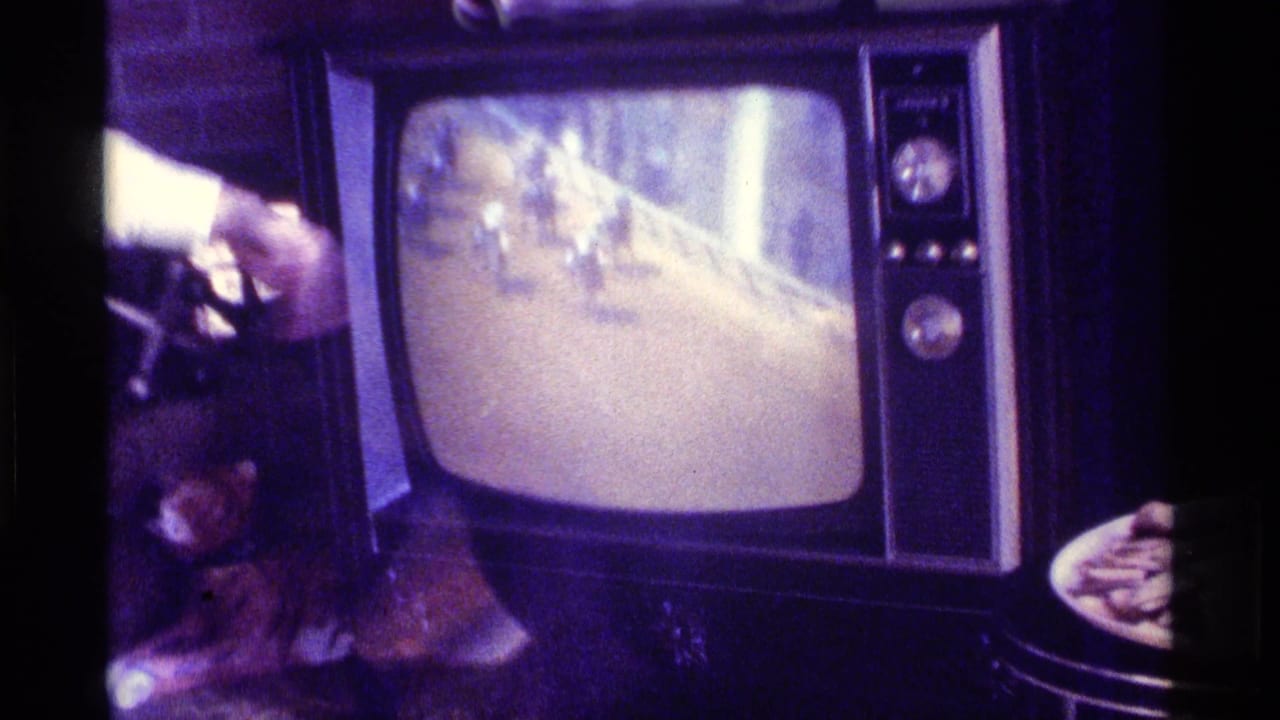 Kentucky 1976 home-movie frame of a CRT television showing a horse race while partial viewers stand or sit close by in a dim private interior.