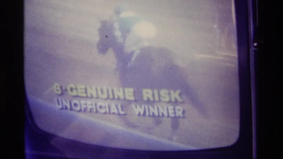 Soft 8mm frame of a Kentucky television horse race broadcast, with a horse and jockey above text naming Genuine Risk unofficial winner.