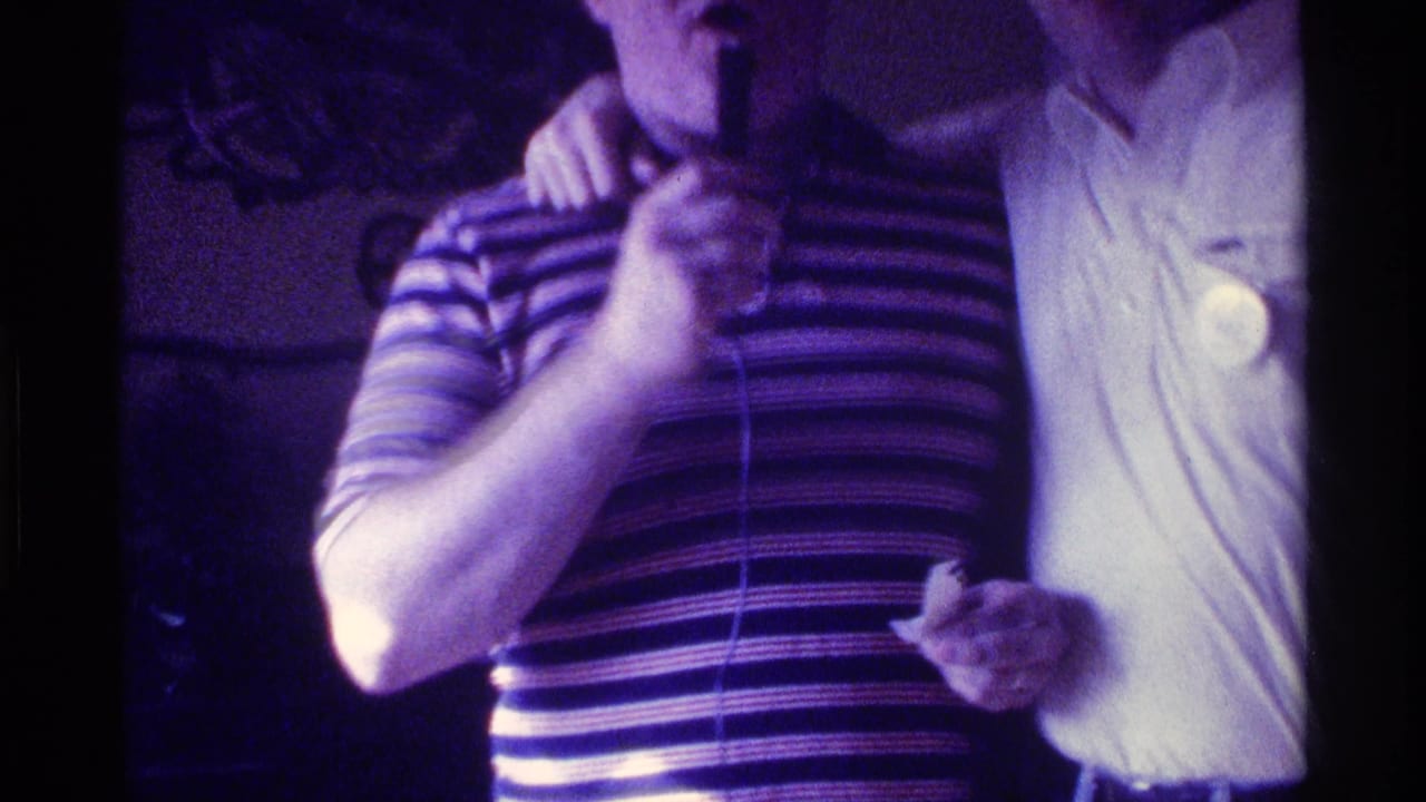Man in striped shirt holds a microphone beside a smiling man in a white shirt.