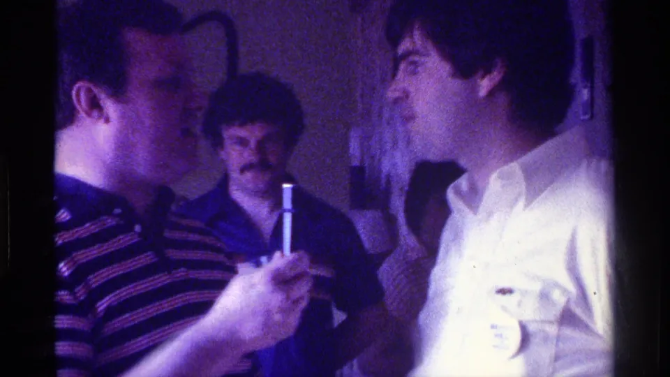 At the end of the clip, the microphone holder stands close to a man in a white shirt, with other adults partly visible behind them.