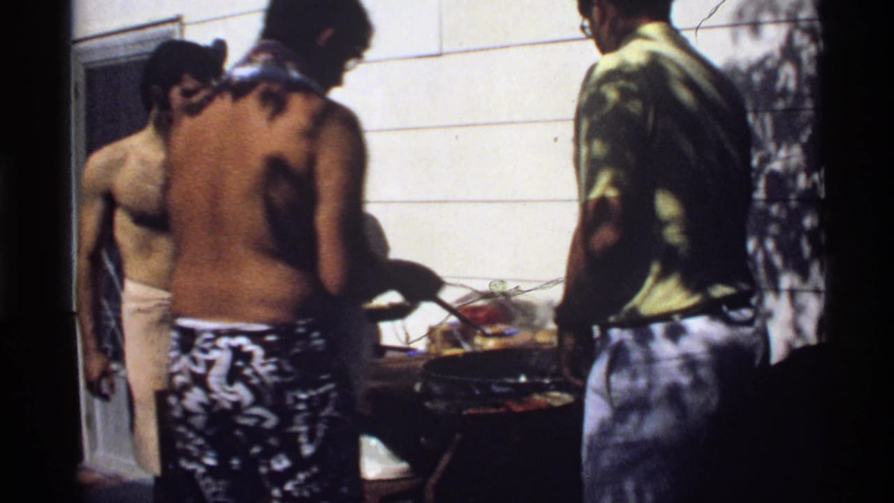 Shirtless men and another adult stand by a backyard grill during a 1978 California home-movie cookout.