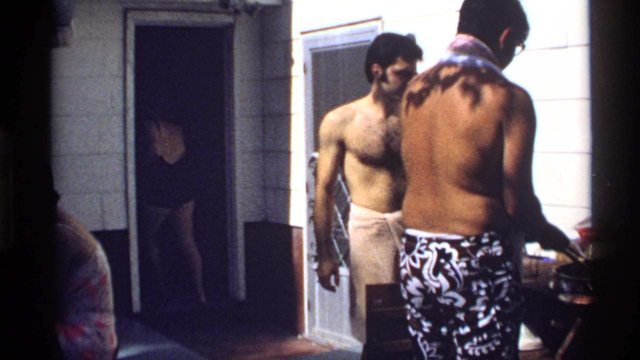Shirtless men in swimwear stand beside a backyard grill and house doorway in 1978 California home-movie footage.
