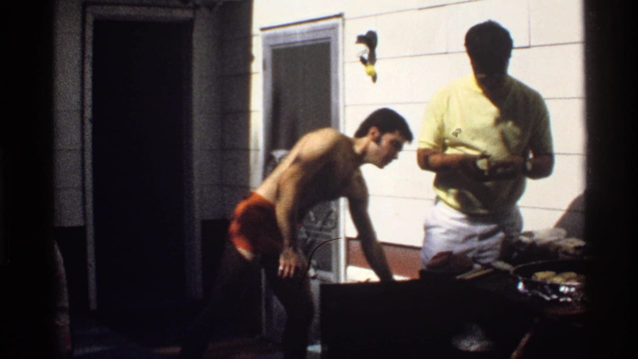 1978 California 8mm frame showing one shirtless man and one man in a yellow shirt preparing food at an outdoor grill.