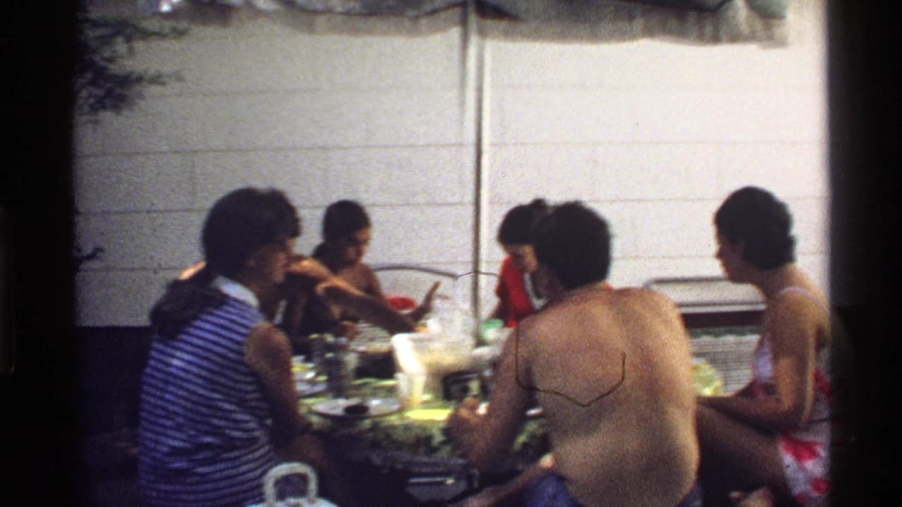 Adults sit around an outdoor table with food and drinks.