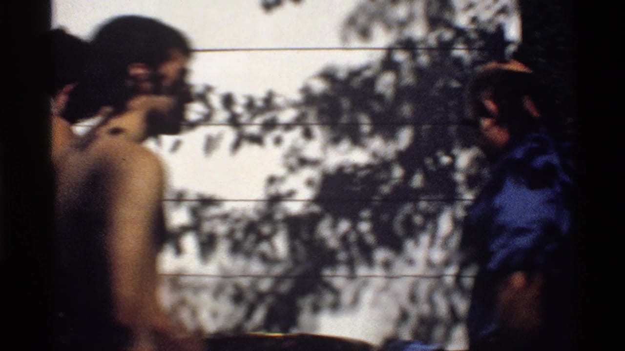 Young men gather by a tiled wall, with one figure in a blue shirt at the right edge.