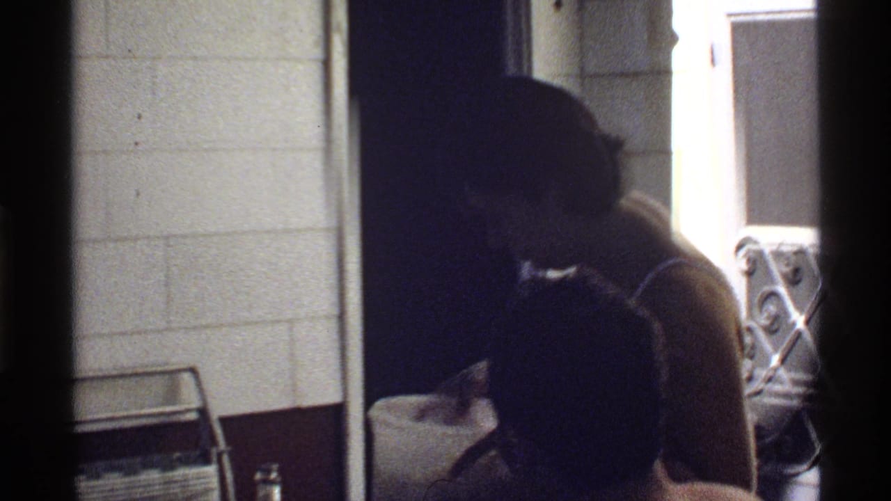 1978 California poolside home-movie frame showing a shirtless person bending near a doorway and patio furniture in dim exposure.