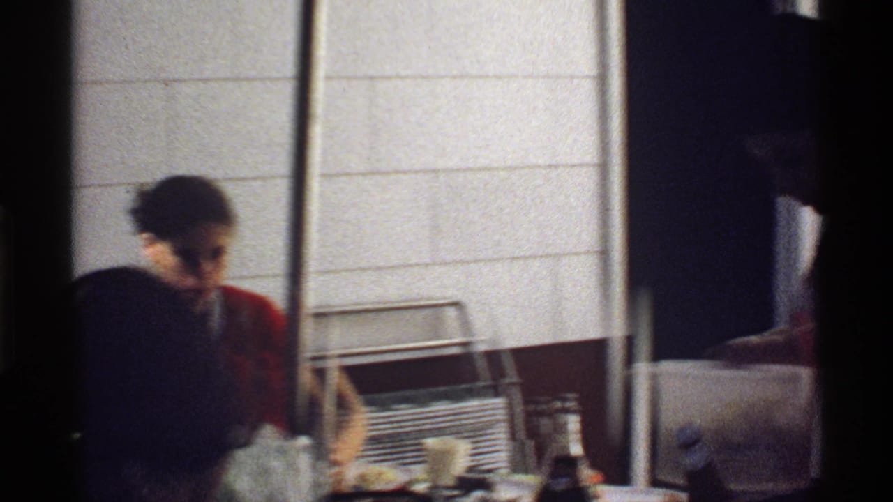 Adults seated at a dining table with plates and glasses near a white block wall.