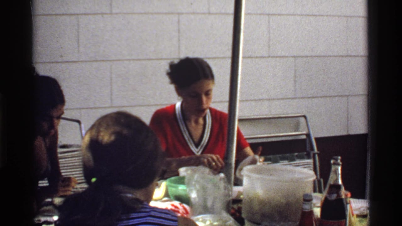 Late-1970s home-movie frame showing young adults at a casual California meal with plastic containers and bottles on the table.