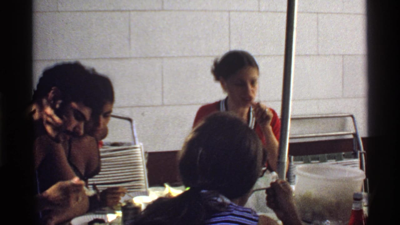 1978 California 8mm frame of young adults eating at a crowded indoor table, with soft focus and handheld framing.