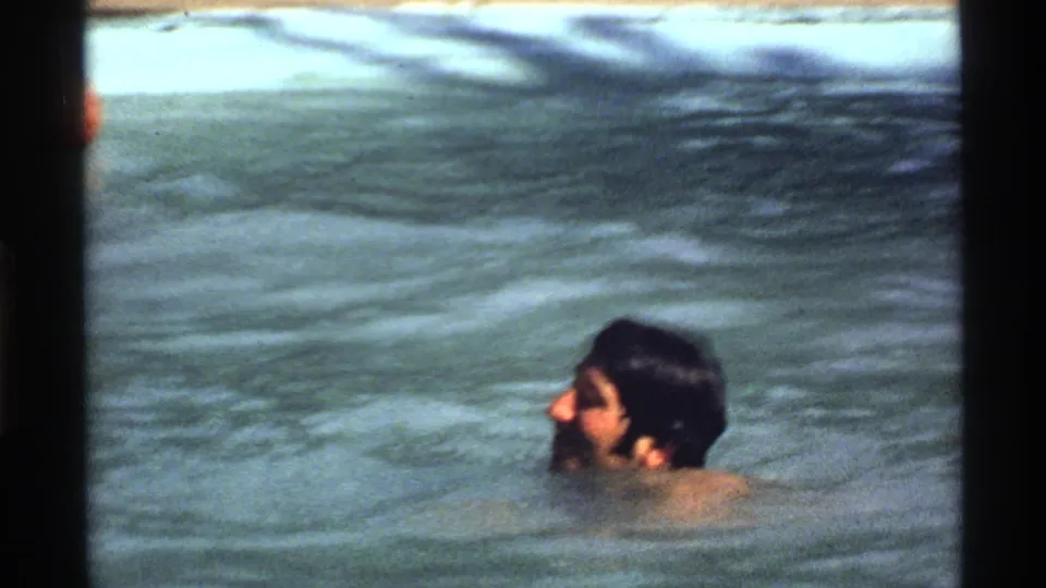 Adult man in profile in a California backyard pool, captured in soft, faded 8mm home-movie footage.