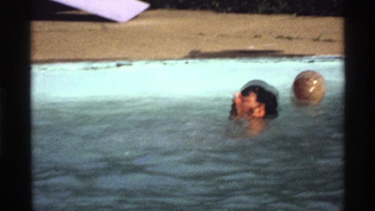 1978 home-movie frame of a man swimming near a ball in a backyard pool, suggesting casual water polo play.