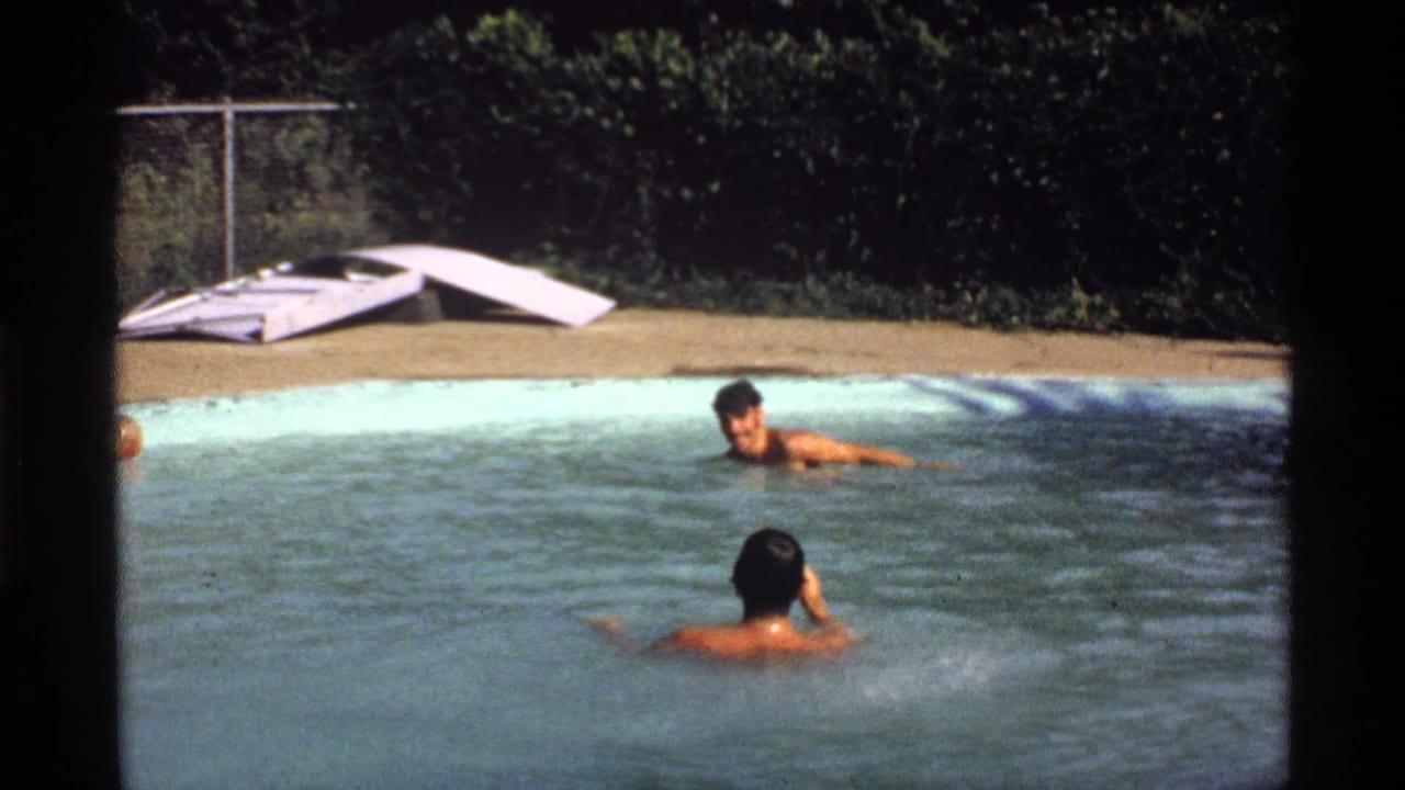 1978 California 8mm frame showing two young men swimming in a backyard pool, with a white diving board and fence in the background.