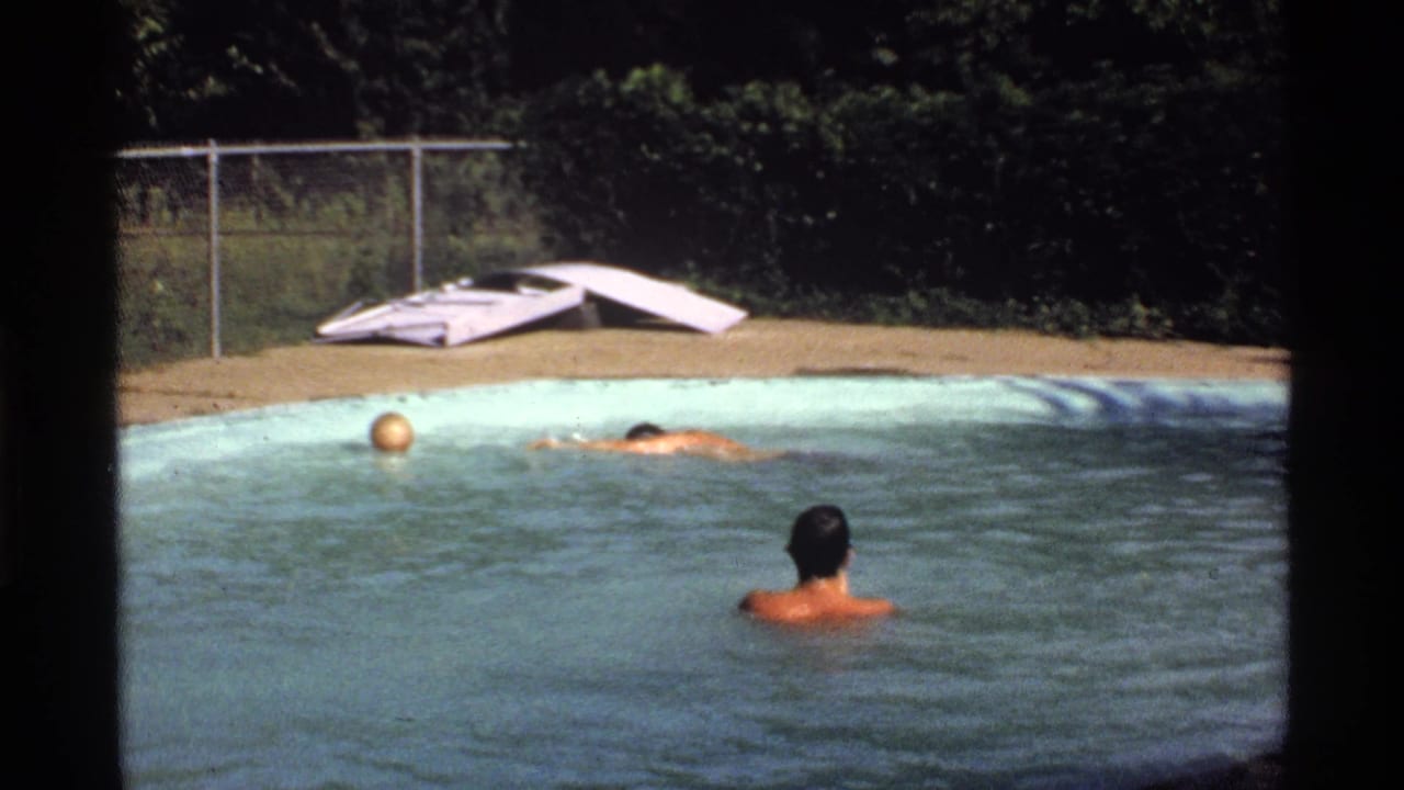 Three men in a backyard swimming pool with a yellow ball near the waterline.