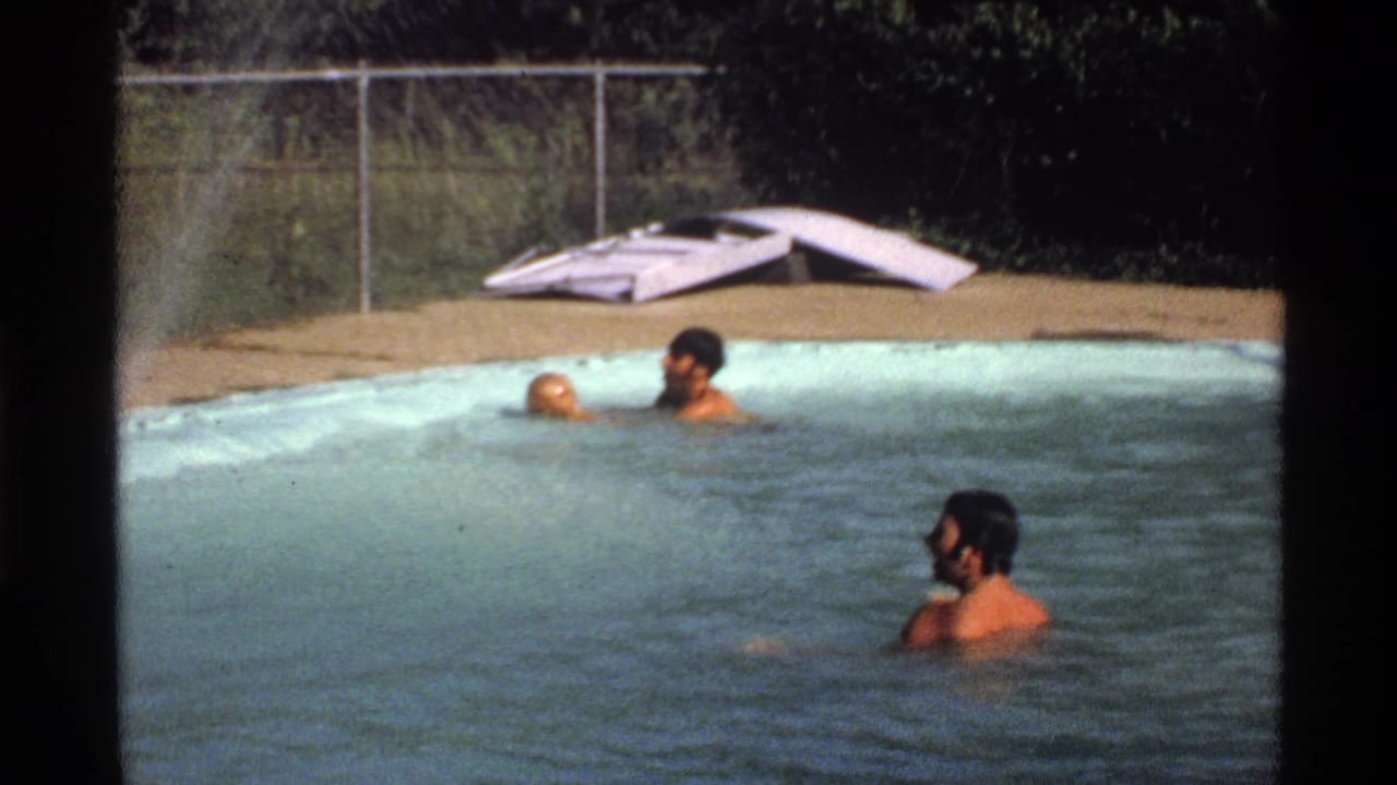 1978 California 8mm frame showing two adult men in a backyard swimming pool, one near a floating yellow ball, with fence and pool deck visible.
