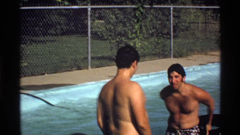 One swimmer is seen from behind while another sits by a black inner tube in the pool during a 1978 California home movie.