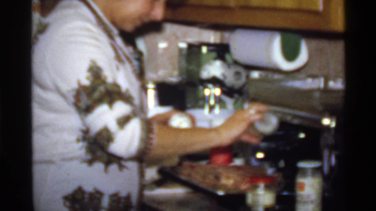 Close view of a woman adding seasoning near a dish on a kitchen counter.