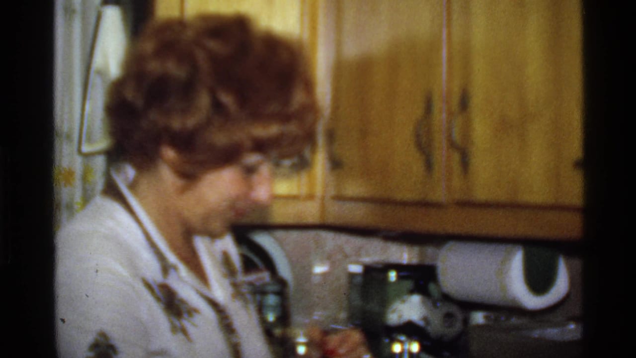 Woman looks down while working at a kitchen counter beneath wood cabinets.