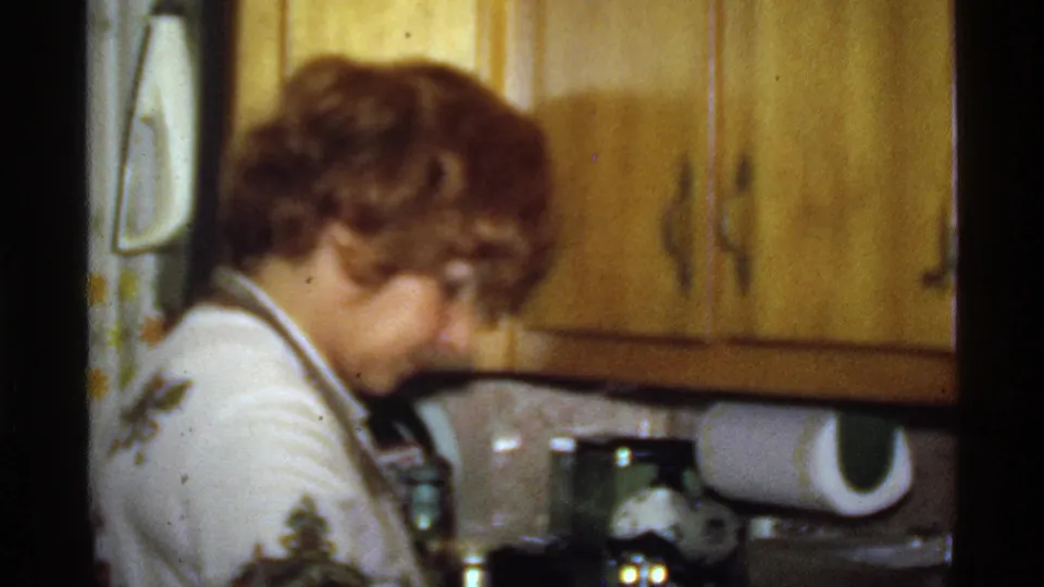 Woman leans over the counter in a 1978 home kitchen, with wood cabinetry and household items in view.