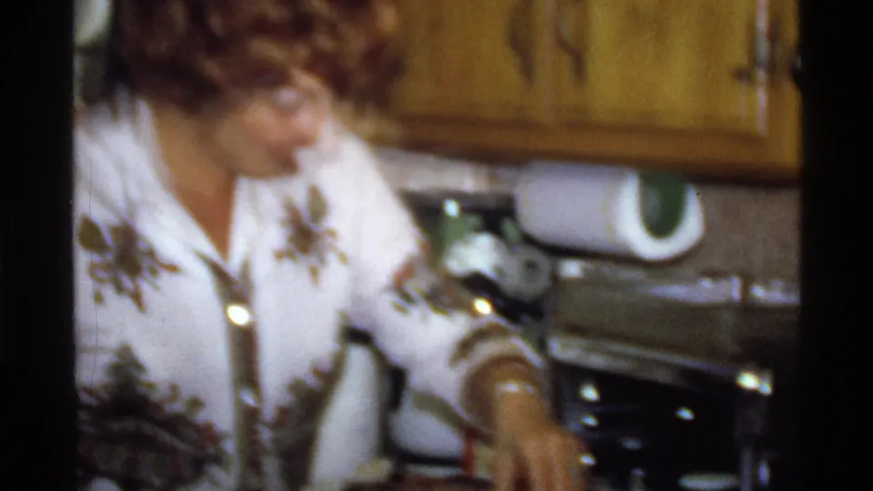 Woman reaches toward the counter in a warm, soft-focus 1978 California kitchen home-movie frame.