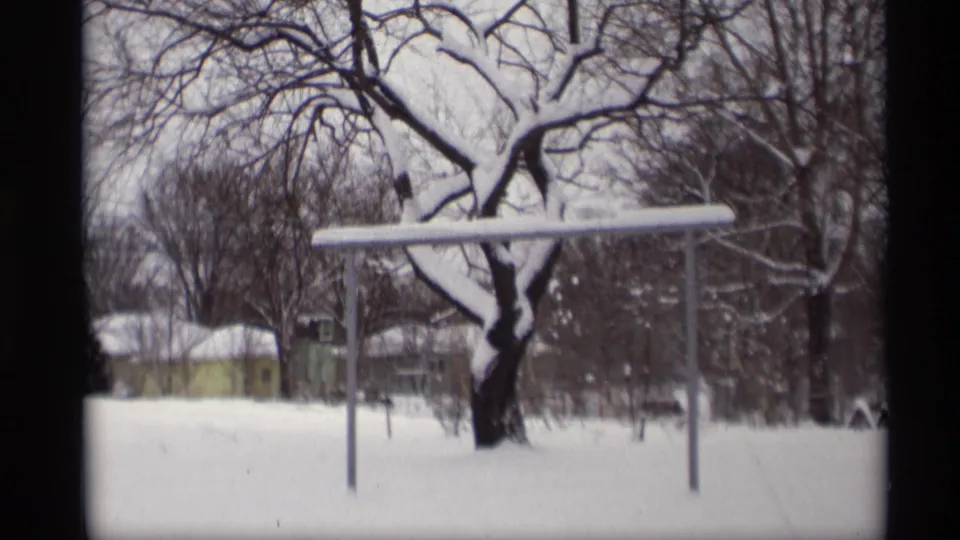 1966 Madison, Wisconsin 8mm frame showing a snowy yard, bare tree branches, metal yard frame, and a yellow house in the background.