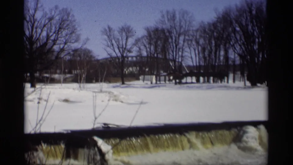 Madison winter landscape from 1966 showing snow, bare trees, a distant bridge, and yellow-tinted water near the frame edge.