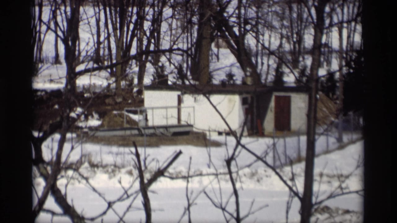 Madison-area 8mm frame from 1966 with a white shed, dark door, bare trees, and thawing snow in the yard.