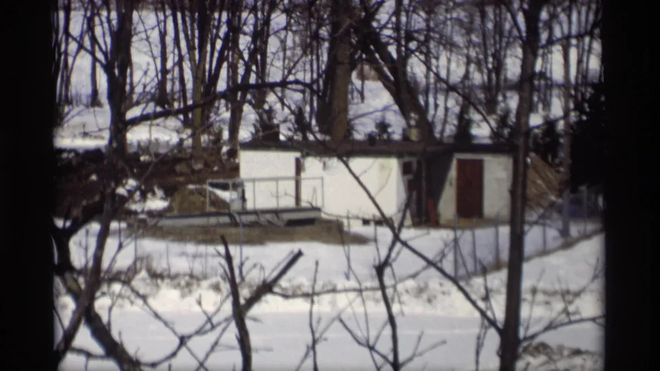 Madison-area 8mm frame from 1966 with a white shed, dark door, bare trees, and thawing snow in the yard.