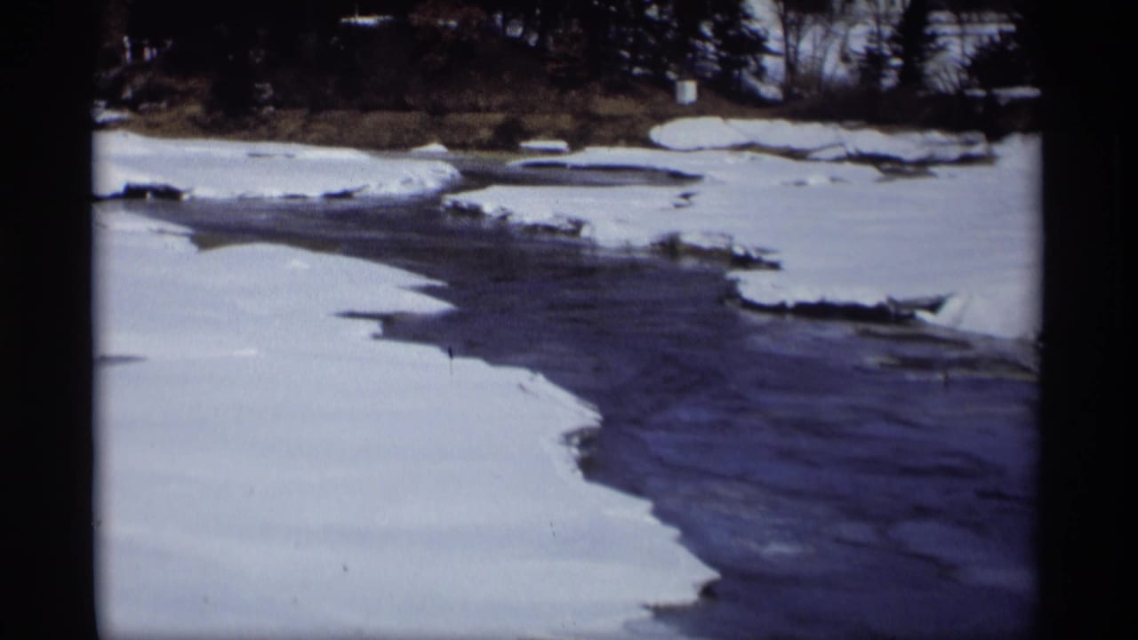 Handheld 8mm view of a snow-lined river bend in Madison, Wisconsin, with open water and broken ice visible in the channel.