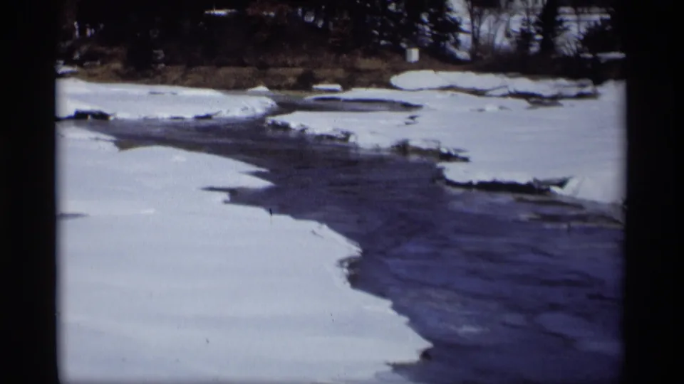 Handheld 8mm view of a snow-lined river bend in Madison, Wisconsin, with open water and broken ice visible in the channel.