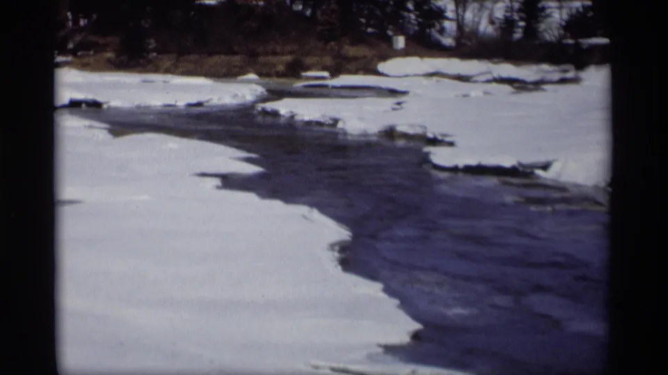 Madison, Wisconsin winter river view from 1966, showing snow, ice, and dark water beneath a bare treeline in home-movie footage.