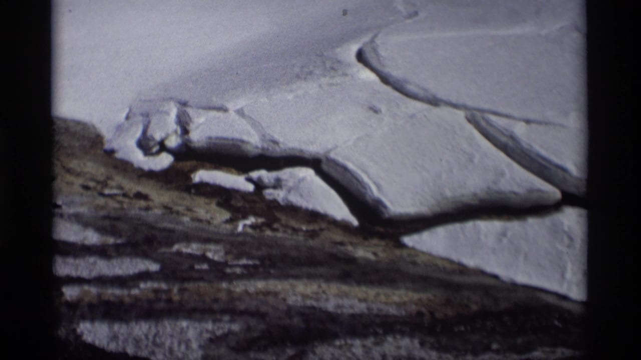 1966 Madison, Wisconsin home-movie frame showing snow, exposed soil, and dark thaw lines across a winter field.