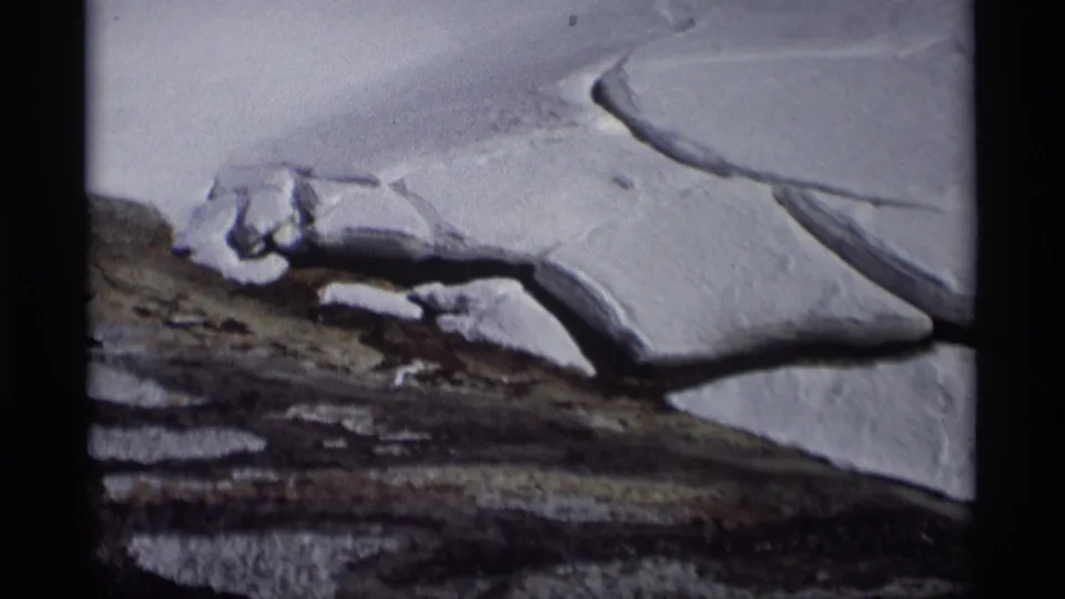 1966 Madison, Wisconsin home-movie frame showing snow, exposed soil, and dark thaw lines across a winter field.