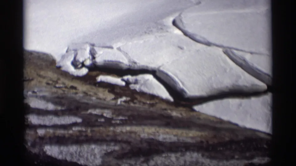 1960s 8mm view of a Madison winter field, with snow cover interrupted by exposed ground and a dark melt line.
