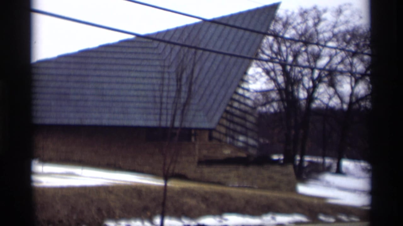 Triangular-roof building seen through a dark window frame with snow on the ground.
