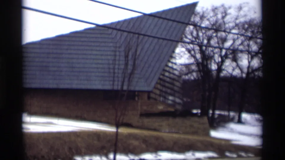 1966 Madison exterior view of a large triangular-roof building, bare trees and snow patches seen through a window frame.
