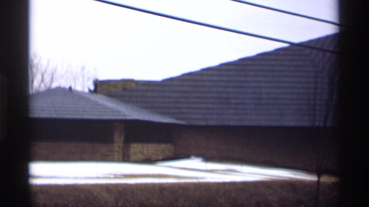 Low stone building with broad sloped roof, snow patches and utility lines overhead.