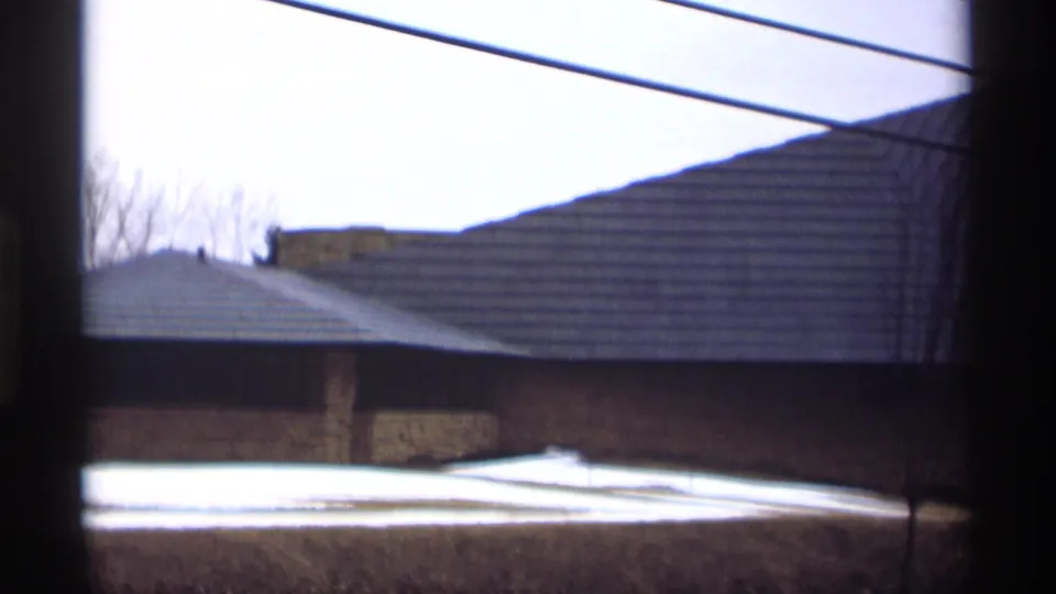 1966 Madison shot of a low stone building with a broad triangular roof, framed by dark window edges and winter snow.
