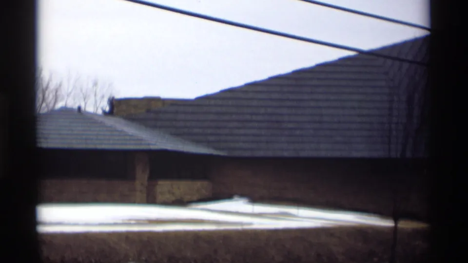 1966 Madison frame showing the broad roof plane and stone facade of the building behind a window and overhead lines.