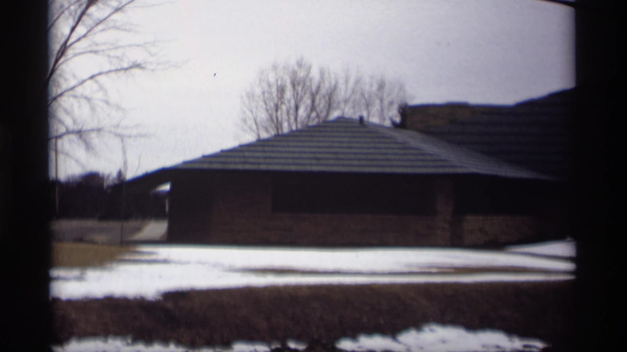 1966 Madison, Wisconsin 8mm frame showing a snow-dusted exterior with bare trees and a low brick building beyond dark foreground framing.